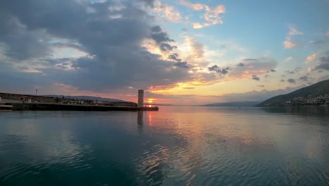 nubes corriendo en una cálida puesta de sol sobre un pequeño faro en la bahía de senj, croacia