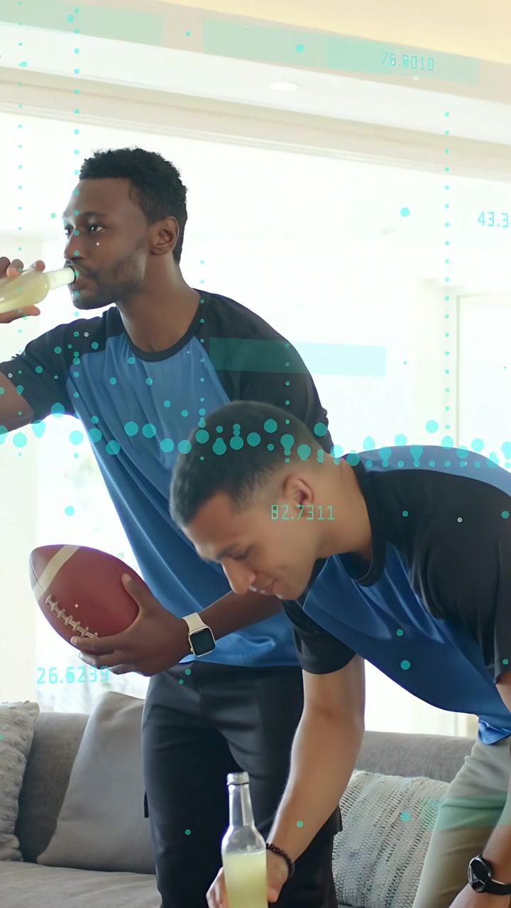 Vertical video: Two men with football and drinks tapping after play leaning in sports data overlay