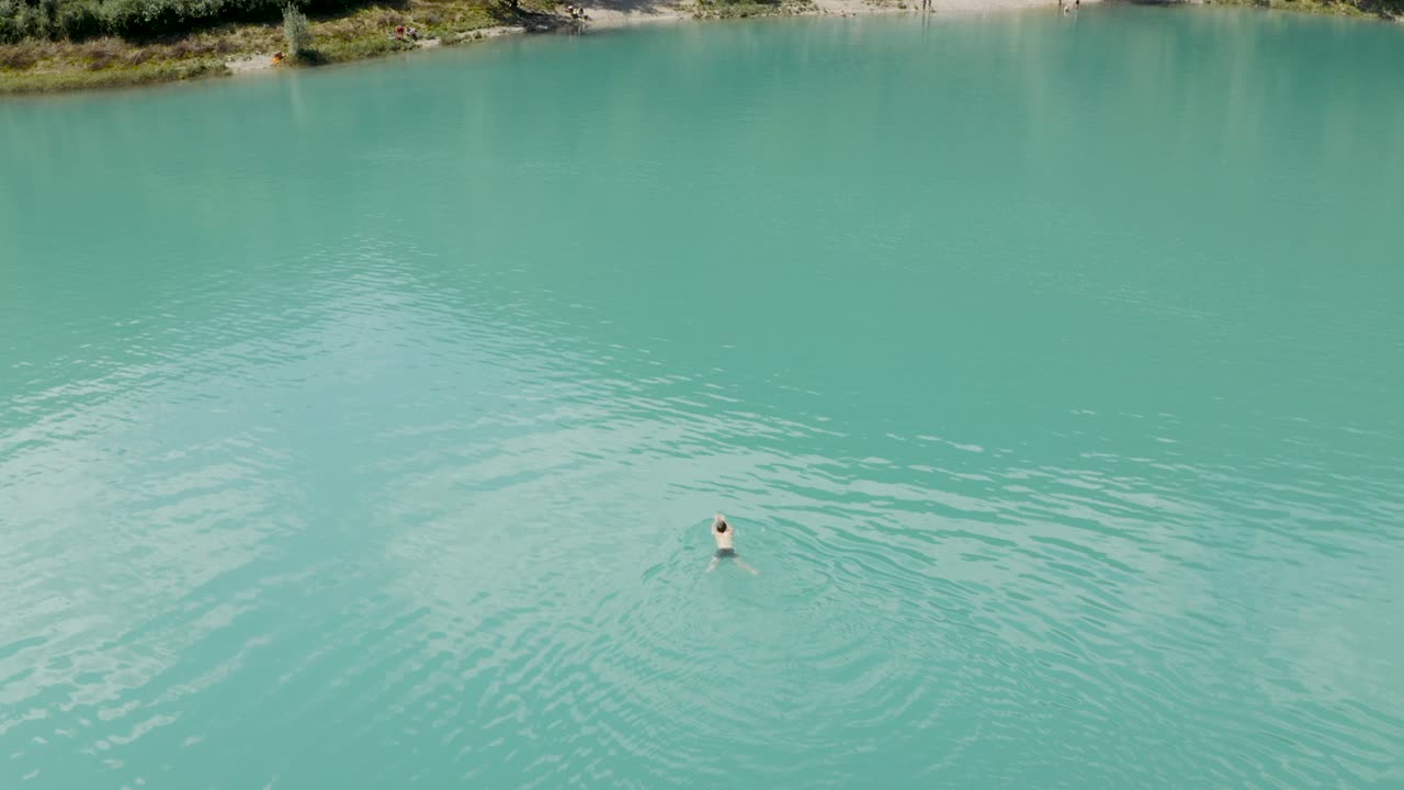 One guy swimming alone in the middle of a green lake on a summer day at Lake Tenno, Italy