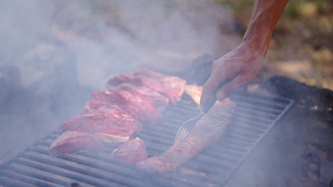 Hand of parrilla chef flips juicy entraña and picaña steaks over smoky wood-fired asado grill, thick smoke rising, authentic outdoor Argentine barbecue scene, focus on meat, hand, and grill, real time
