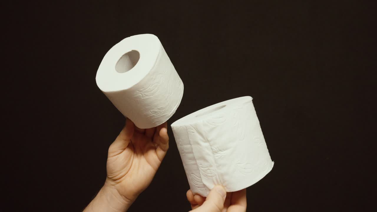 hands holding two toilet paper rolls against a dark background. Concept of bathroom hygiene, household supplies, sanitation, and everyday essentials