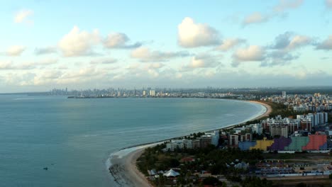 Beautiful-aerial-drone-shot-of-the-tropical-city-of-Joao-Pessoa-with-a-large-coastline-and-skyscrapers-in-the-distance-behind-a-bunch-of-palm-trees,-located-in-Northern-Brazil