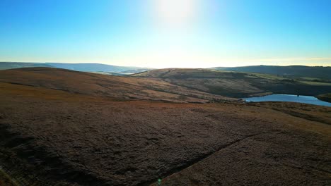 Imágenes-Aéreas-De-Invierno-Volando-Sobre-Páramos-Dorados-Directamente-Al-Sol-Con-Lago,-Embalse-En-La-Distancia