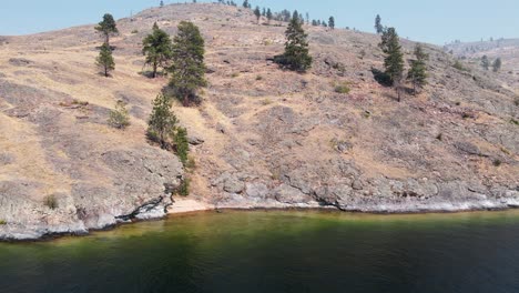 a steep, rocky cliff falling into okanagan lake with one lonely boat anchoring near the shore