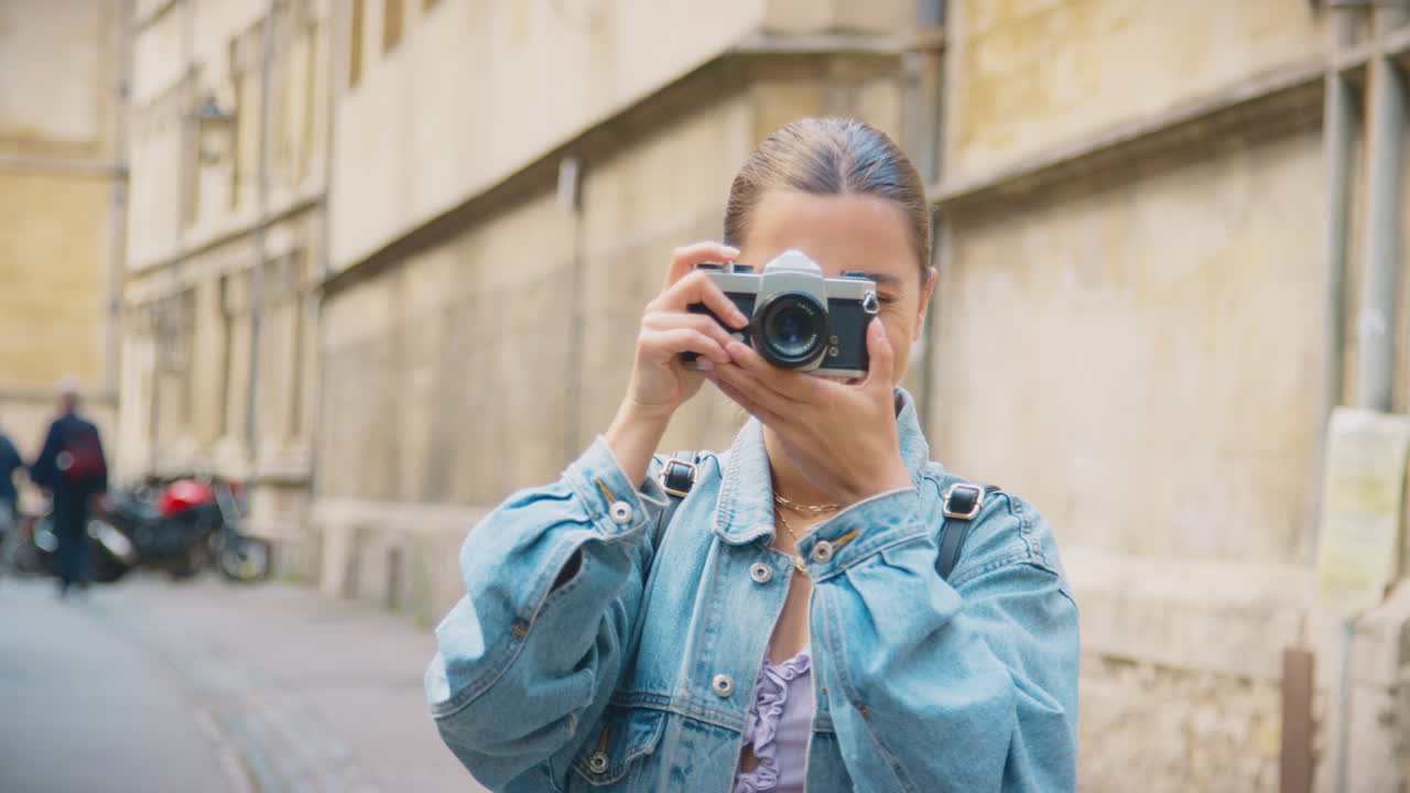 mujer joven en la calle de la ciudad tomando una foto con una cámara digital de estilo retro para publicarla en las redes sociales