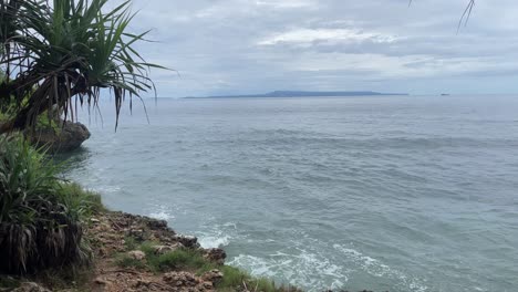 steady shot of an ocean scape as waves hitting, water splashing on the seashore, island in the distance