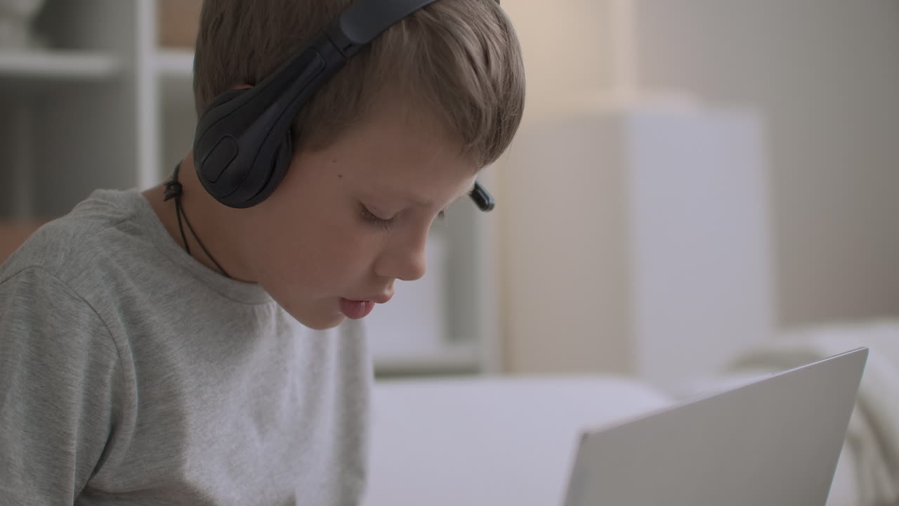 el niño de la escuela está escuchando cuentos de hadas a través de auriculares por cuaderno y dibujo sentado a la mesa solo en la habitación