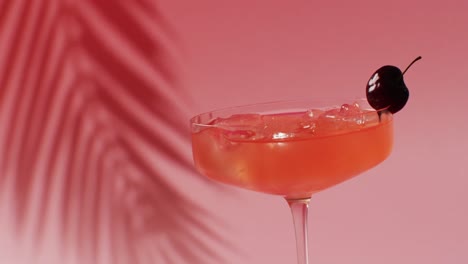 Close-up-of-drink-with-cherry-on-pink-background