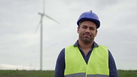 portrait of latin professional man standing on wind turbine field.