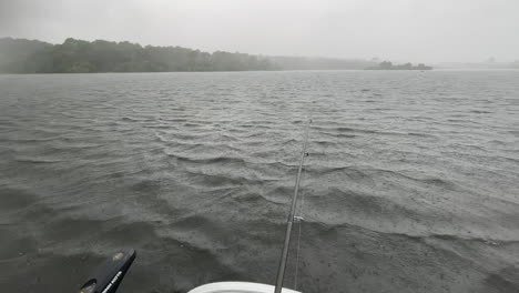 pov: a man is fishing on a boat in the middle of a lake and a storm, heavy rain falls on the water