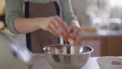 close-up of cracking raw egg into bowl preparing dough