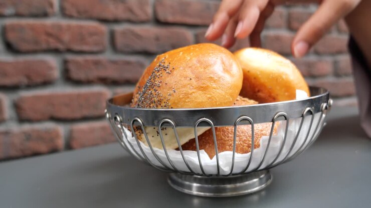 A hand reaching for a fresh baked bun in a basket on a table