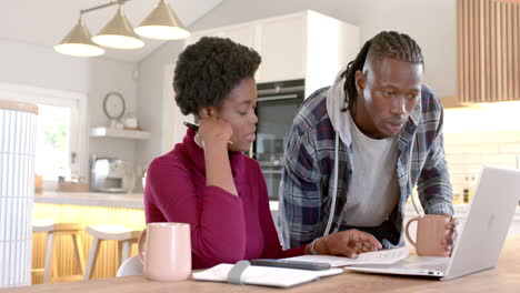 Working together, African american couple using laptop and discussing documents at home