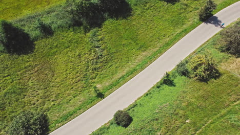 Topshot-of-a-cyclist-in-blue-riding-on-an-empty-countryside-road,-surrounded-by-lush-green-meadows