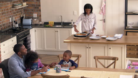 father and children drawing at table as mother prepares meal