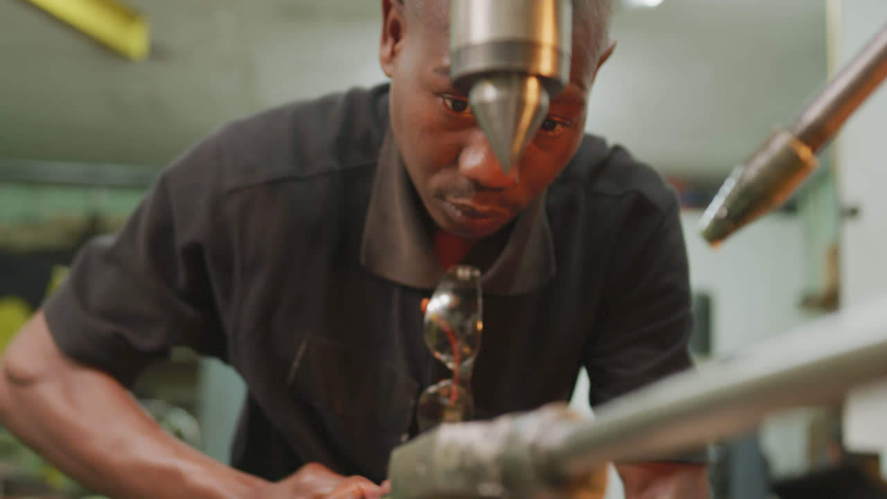 African American male factory worker at a factory standing at a workbench and operating machinery