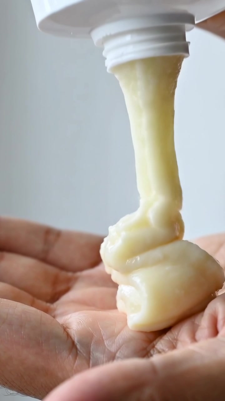 Vertical video: Pressing white tube, hands squeezing pale-yellow cream into open palm in close-up