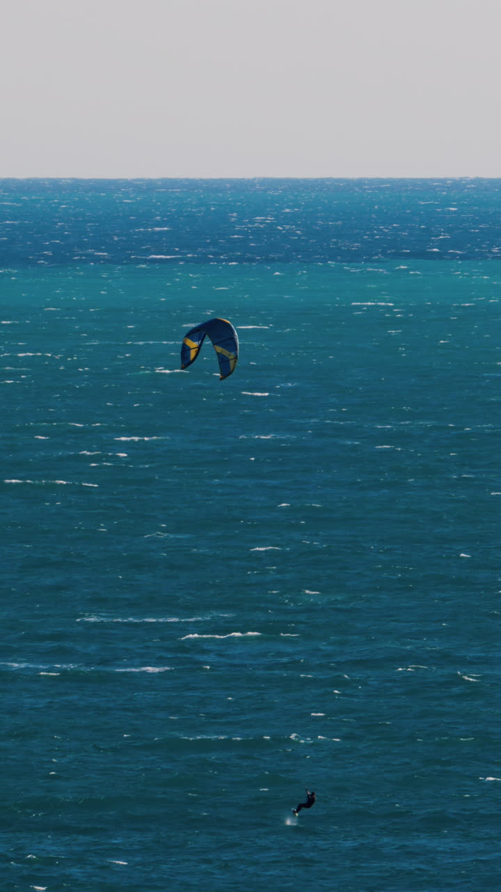 Distant view of a man kitesurfing on a sunny day. Vertical