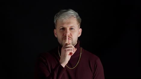 man with blonde hair and blue eyes holding finger to lips