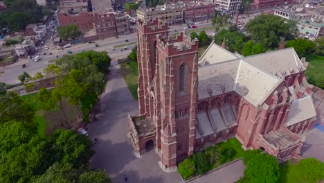 Vista-Aérea-Superior-De-Un-Hermoso-Edificio-De-La-Iglesia,-El-Tráfico-Se-Mueve-En-El-Otro-Lado-De-La-Calle-De-La-Iglesia,-Hermosa-Vegetación-Alrededor-De-La-Iglesia