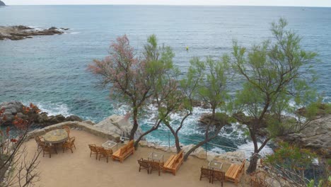 Cala-Banys-En-Lloret-De-Mar-Vistas-A-La-Playa-Rocosa-Mar-Mediterráneo-Aguas-Transparentes-Azul-Turquesa-Espectacular-Restaurante-En-Primera-Línea-De-Mar-Con-Sillas-Chill-Out-Con-Vistas-Directas-Al-Acantilado