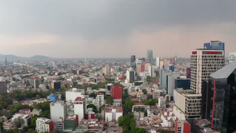 Backwards-flying-drone-camera-over-town.-Low-residential-houses-neighbors-with-tall-office-buildings.-Cityscape-view-before-rain.-Mexico-city,-Mexico.