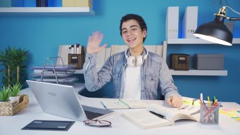 young student looking at camera while studying and waving at camera while smiling.