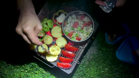 Un-Hombre-Mochilero-Parrilla-Patata-Pollo-Verdura-En-Barbacoa-Cocinar-Comida-En-La-Naturaleza-Salvaje-Desierto-Supervivencia-Carbón-Fuego-Leña-Hoguera-Deliciosa-Comida-En-La-Noche-Oscura-En-El-Campamento