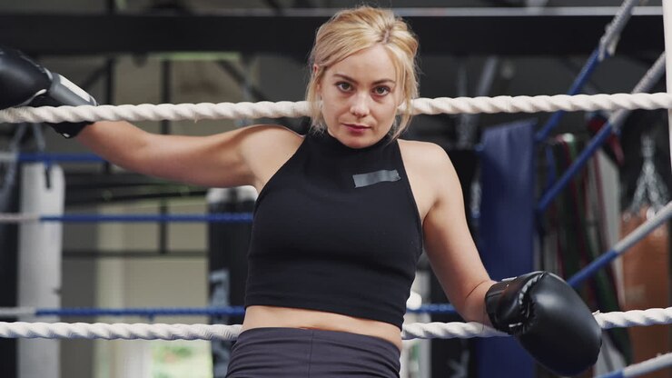 retrato de una boxeadora con guantes en el gimnasio sentada en el ring de boxeo