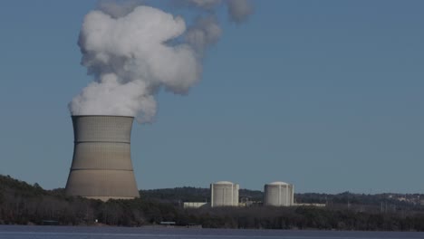 nuclear stack emitting steam in real time on a sunny and cloudless day with lake in the foreground