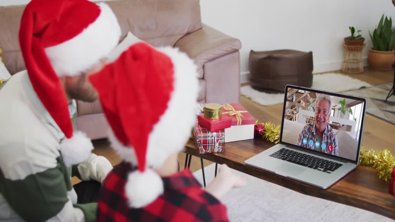 padre y hijo caucásicos usando sombreros de santa en una videochat portátil durante la navidad en casa