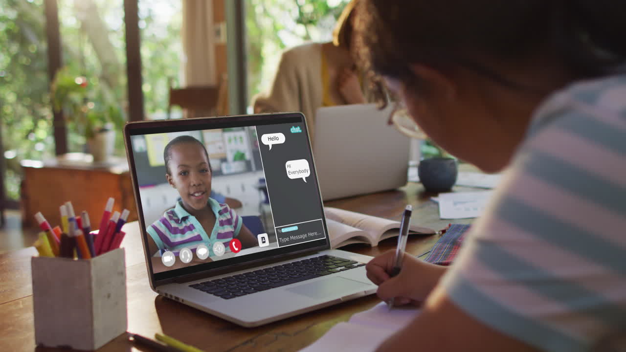 Schoolgirl using laptop for online lesson at home, with her colleague and web chat on screen