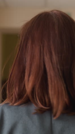 Close up back shot of woman walking purposefully down modern hallway, holding red folder, dressed in professional attire, exuding confidence and determination