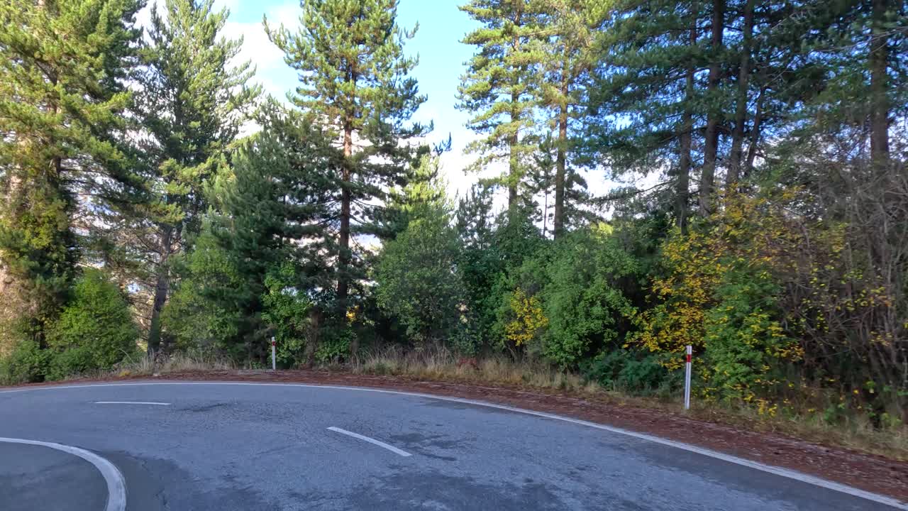 Vehicle travels winding forest road with mountain views, daylight, smooth camera movement, serene atmosphere