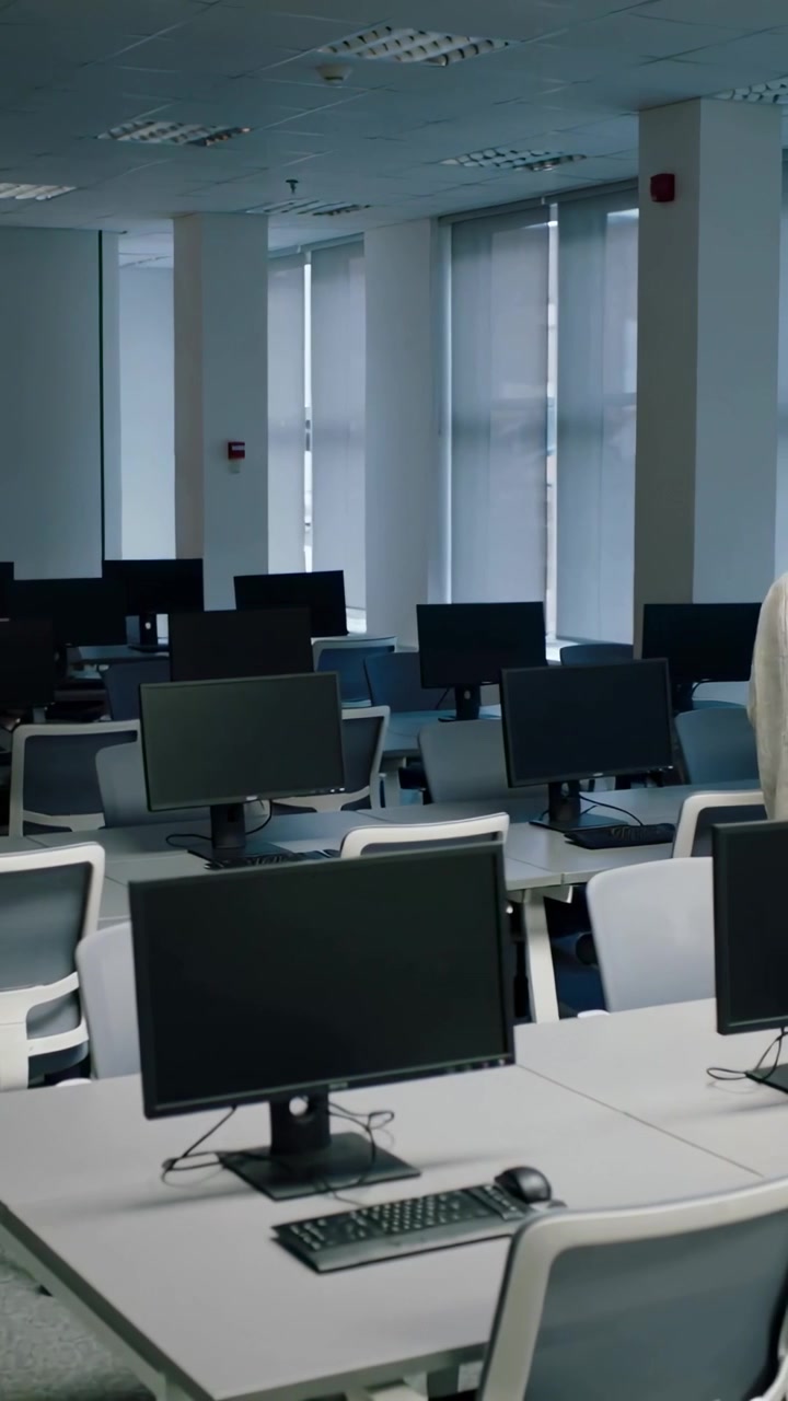 Vertical video: Entering man in beige knit holding laptop walking past lab monitors, copy space