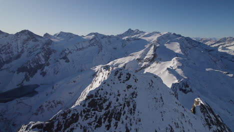 drone flying backwards at snowy austrian kitzsteinhorn mountain peak with large cross on it surrounded by snowy mountain landscape on a sunny day