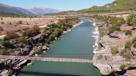 wooden suspension bridge across vjosa river, albania - aerial fly over