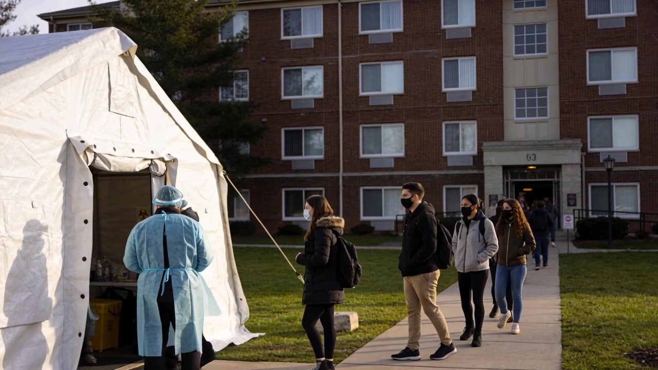 Gli studenti escono dalla porta della residenza e si dirigono verso una tenda bianca, dove il personale effettua controlli con DPI e borse.