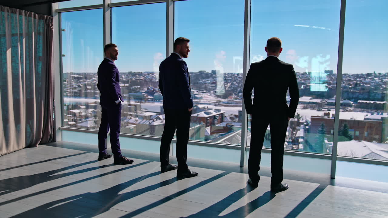 Business partners near windows with city view. Elegant managers in suits having a conversation in the light office room in sunny day. Back view.