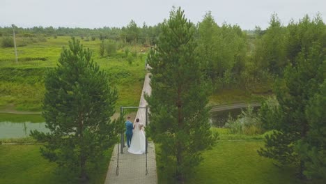 newlywed couple walks to wooden bridge aerial backside view