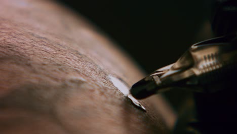 close up tattoo artist demonstrates the process of getting black tattoo with paint on back of a client