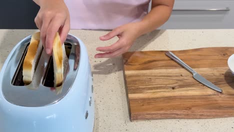 a person inserts two slices of white bread into a blue toaster on a kitchen counter, with overhead lighting and steady camera framing