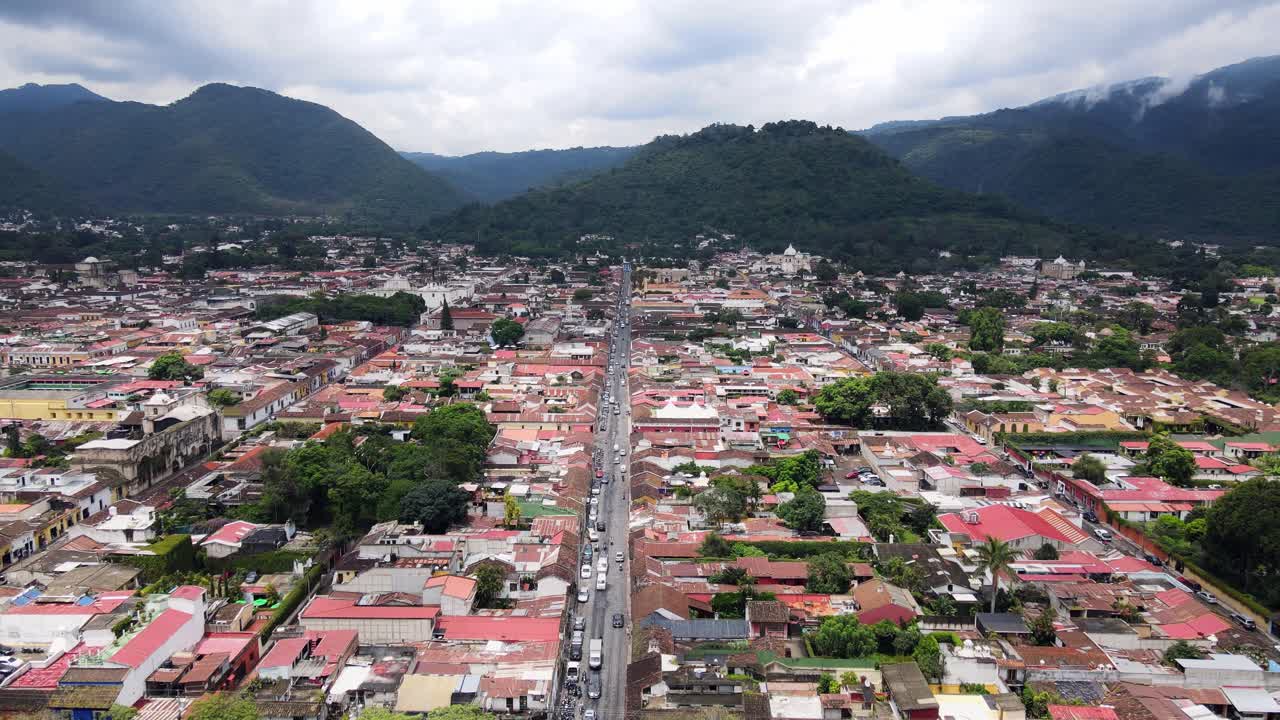 4K aerial drone footage of Antigua, Guatemala, with the cityscape and colorful buildings set against a backdrop of stunning mountains