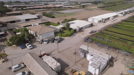 Aerial-view-of-a-tractor-driving-near-fields-of-green-plants-in-a-kibbutz-in-northern-Israel-during-the-summer,-mountains-in-the-background,-parallax-to-the-left