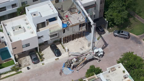 panning tilt down drone shot of a concrete pump pouring cement to make the tile of a house with several workers spreading the material with shovels
