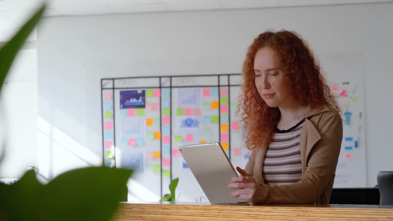 Front view of young caucasian businesswoman working on digital tablet in cafeteria of modern office