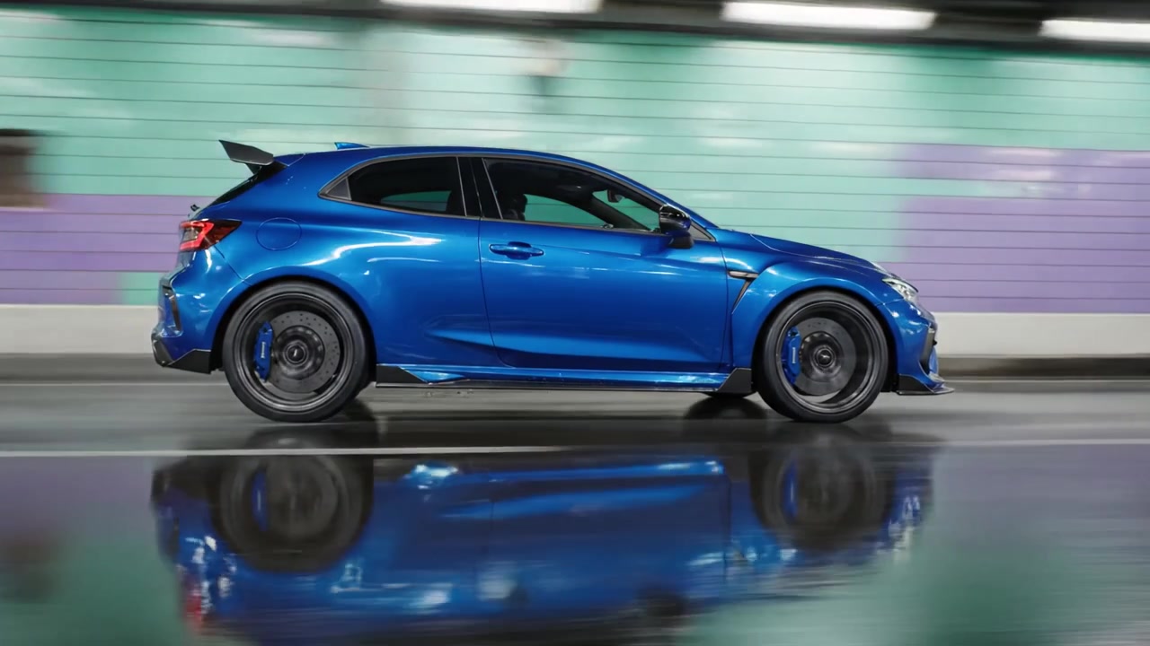 Elegante auto hatchback blu che sfreccia attraverso un tunnel urbano colorato, riflettendo luci vivaci sull'asfalto bagnato, mostrando movimento dinamico e design moderno.