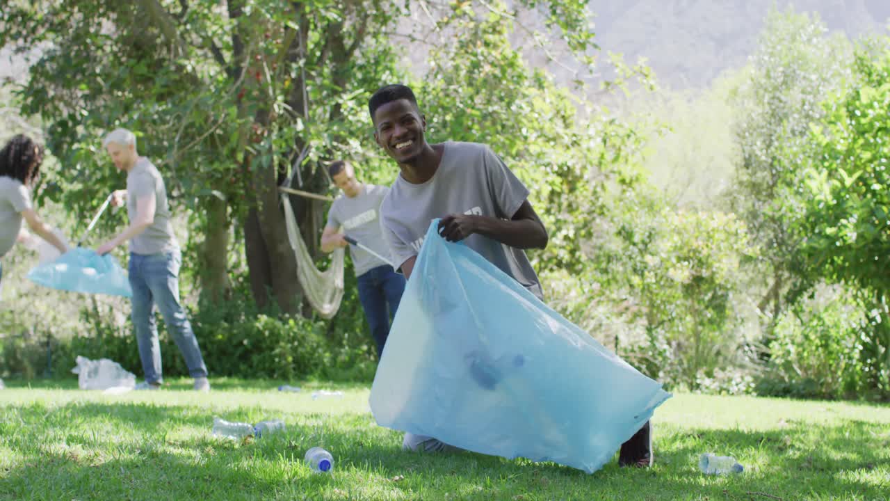 Happy diverse group of friends in volunteer t shirts putting plastic waste in refuse sacks outdoors