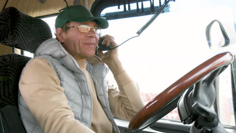 bottom view of caucasian older worker sitting in a truck in a logistics park while talking on the radio