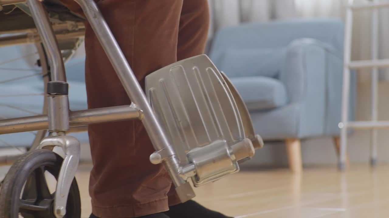 체어에 앉아있는 남성 간호사가 집에서 물리 치료 중에 일어서서 는 환자의 손을 잡고 있습니다.